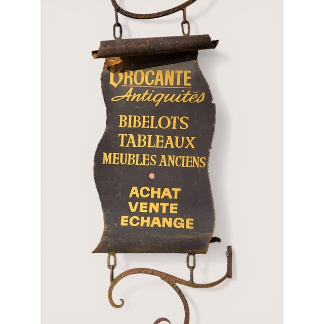 Antique shop sign in patinated metal with wrought iron supports. Designed to resemble a rolled-up scroll and marked...