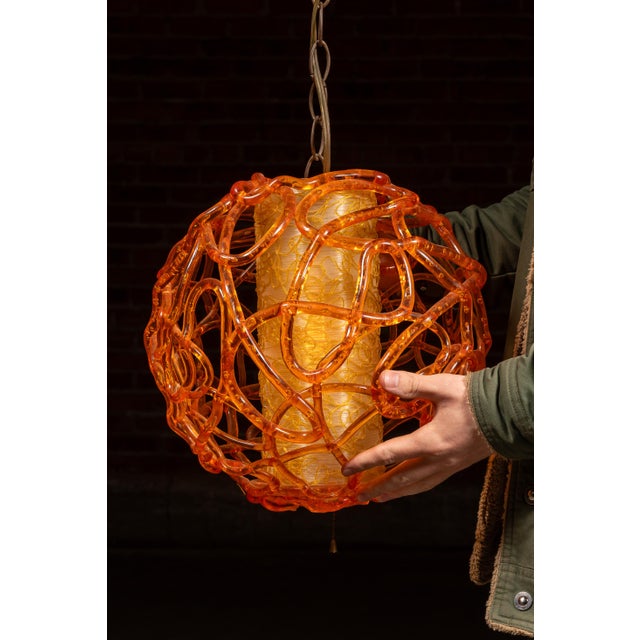 Striking mid-century pendant light featuring an outer globe of translucent amber-orange lucite formed into looping,...