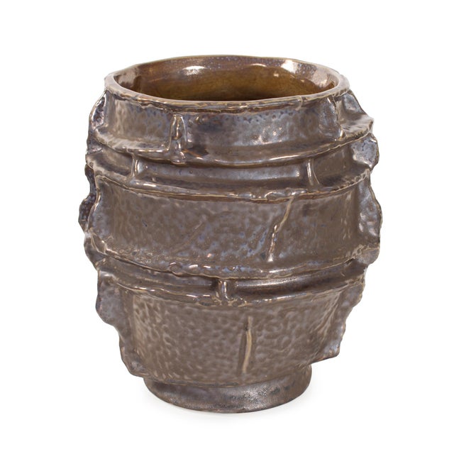 This sculptural ceramic piece features a rugged, layered texture that mimics the strata of ancient rock formations or...