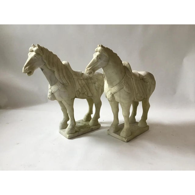 A pair of Tang dynasty style horse figures carved in a pale cream marble with buff tone and light natural veining. The...