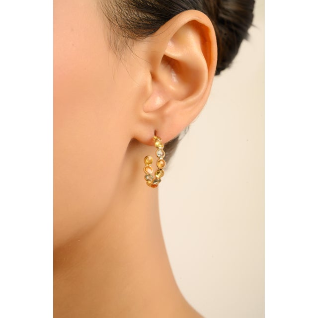 These elegant hoop earrings feature 22 round-cut natural multi sapphires totaling 5.59 carats, meticulously set in rich...