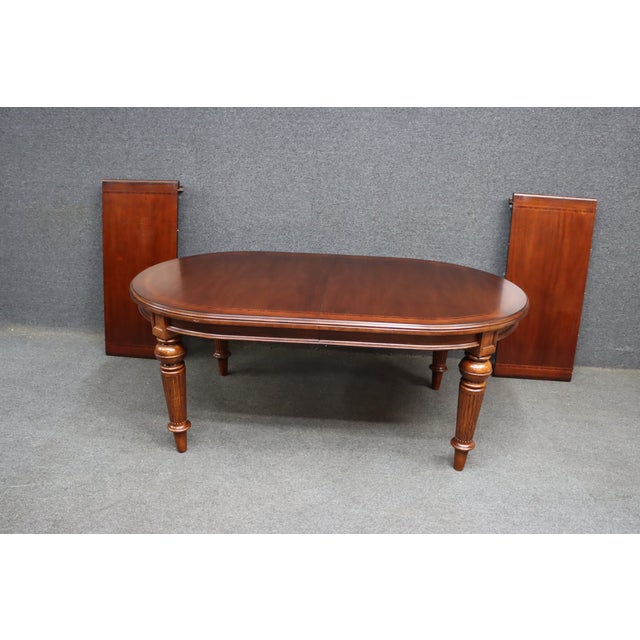A Thomasville attributed cherry dining table featuring an oval top with a satin finish, subtle banded inlay, and turned,...