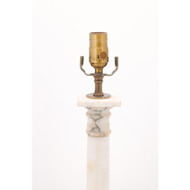 A refined pair of marble column lamps featuring classical Louis XVI wreath ornamentation and stepped bases. The...