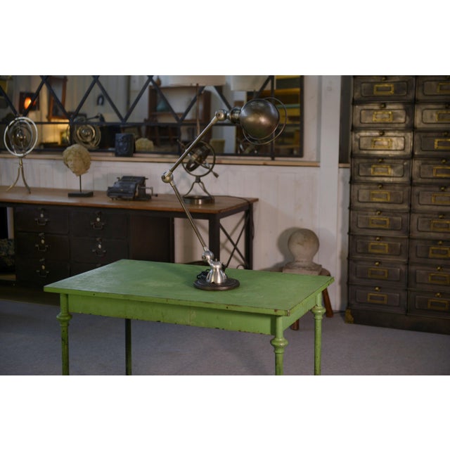 An iconic workshop lamp with two articulated arms and 360° rotating ball joints, a hemispherical shade, and a heavy base,...