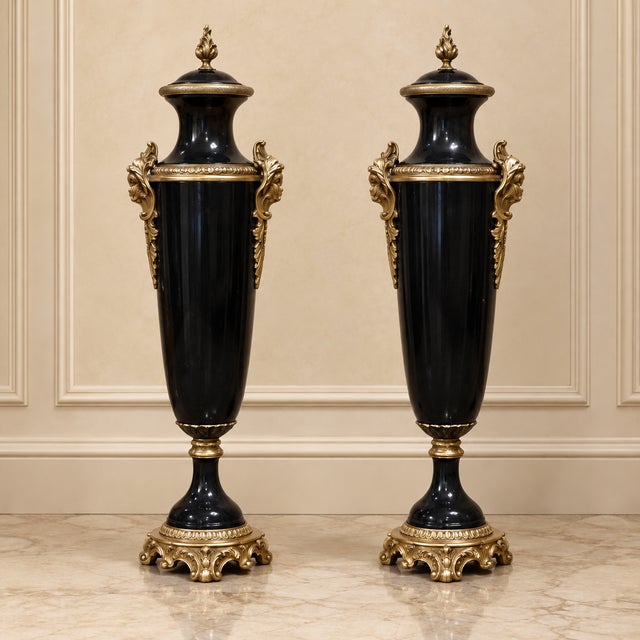 Sophisticated pair of French Empire-style decorative urns featuring a dramatic glossy black finish accented with elaborate...
