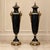 Sophisticated pair of French Empire-style decorative urns featuring a dramatic glossy black finish accented with elaborate...