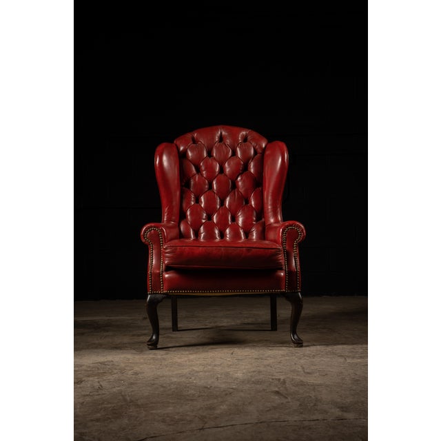 Traditional wingback armchair and coordinating ottoman upholstered in rich oxblood-red leather. The chair features a tall,...