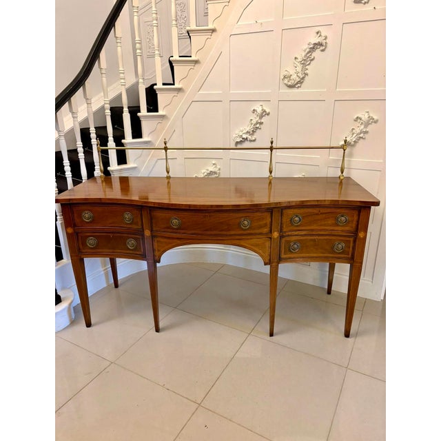 A refined antique Edwardian serpentine sideboard, finely constructed in figured mahogany and enriched with satinwood...