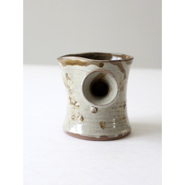 This vintage studio pottery pitcher exudes rustic charm with its hand-thrown form and earthy, textured glaze. The organic...