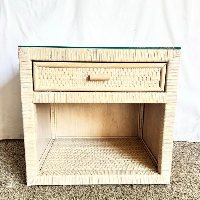 A charming Boho Chic wrapped wicker nightstand featuring a protective glass top over a woven surface, offering both...