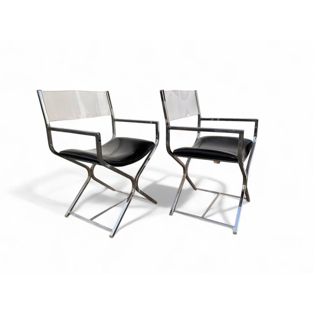 A striking pair of 1970s director’s chairs featuring sleek chrome-plated steel frames, clear lucite backrests, and black...