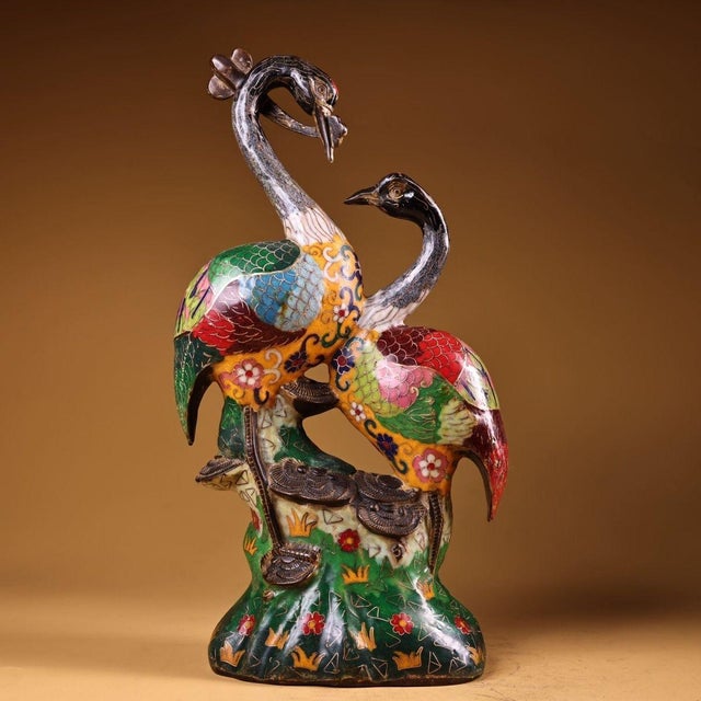 This is a finely crafted cloisonné enamel figurine featuring a pair of cranes perched on a stylized, rocky base. The...