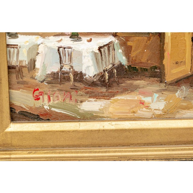 A charming signed oil on canvas depicting a sunlit terrace café scene, with white-clothed tables set beneath a warm red...