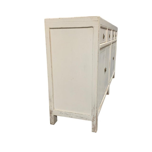 A distressed whitewashed finish sideboard with four cabinet doors and four drawers, offers a rustic and charming addition...