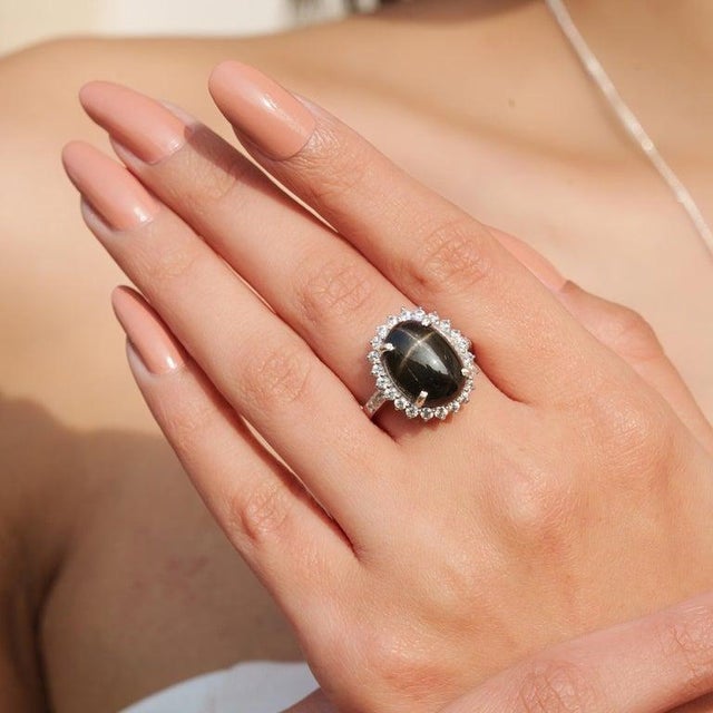 Featuring a 10×14 mm oval-cut black star gemstone weighing 9.1 carats, accented with zircon stones weighing 1.40 carats,...