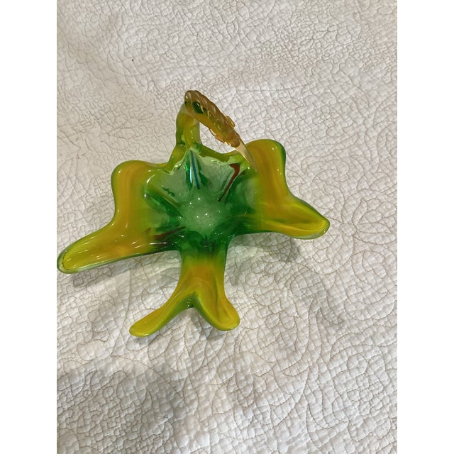 A Murano glass bird candy dish. Bird has its head turned as if preening. Primary colors are green and gold.
