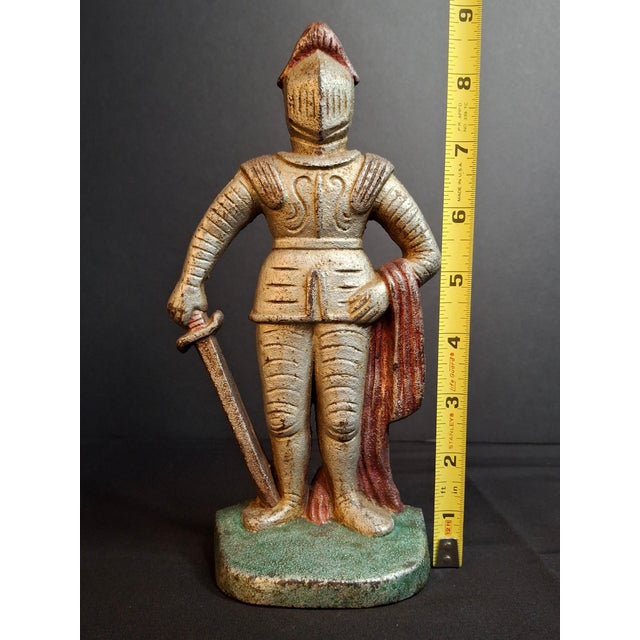 This antique cast iron figural doorstop depicts a standing knight in full suits of plate armor with a lowered visor,...