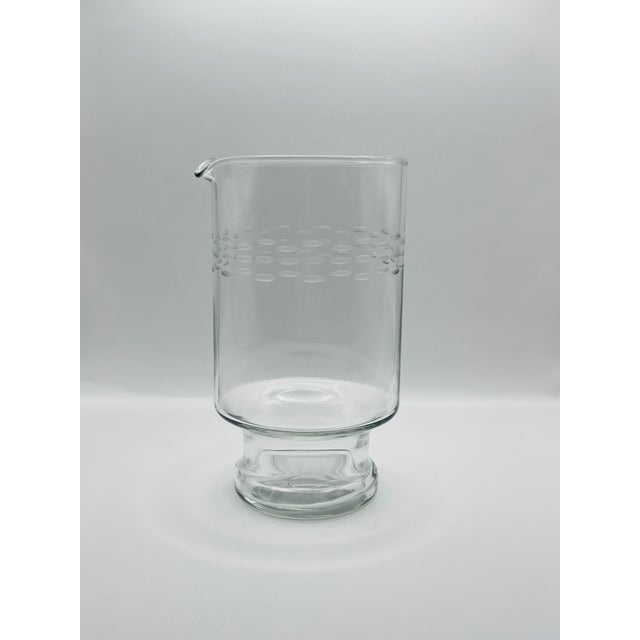 A clear glass footed water carafe decorated with three bands of etched dots with an ice lip for ease of pouring.