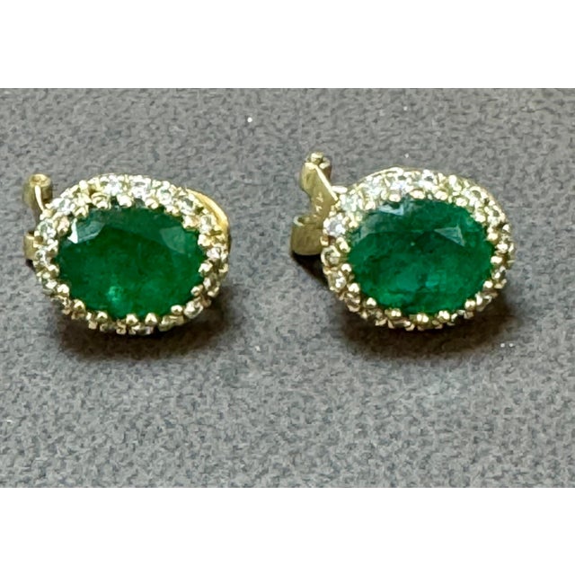 These stunning post back earrings with French clip feature a natural oval-shaped emerald weighing total approximately 5...