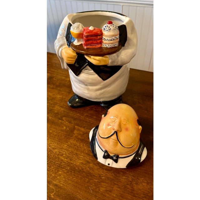This cookie jar features a hand-painted caricature of a butler or waiter with a whimsical, nostalgic expression. He is...