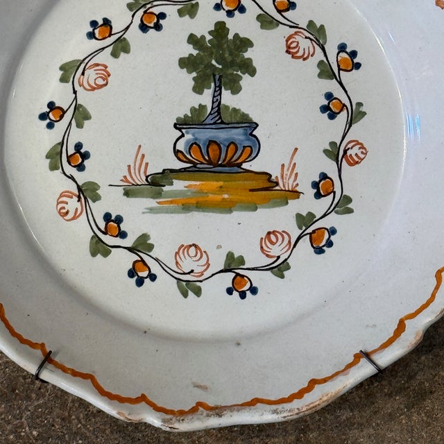 A shaped-rim Delft plate painted with a central urn and topiary tree motif surrounded by a circular garland of roses and...
