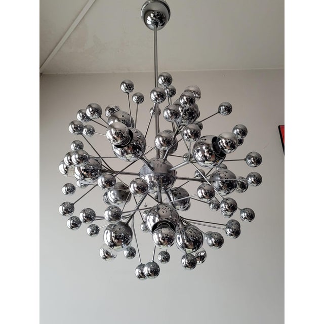 An iconic pendant lamp featuring a dynamic, sculptural structure composed of a central sphere from which numerous metal...