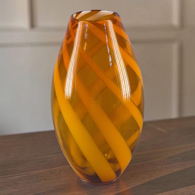 This Mid-Century Modern hand-blown cased glass vase features a warm amber and white ribbon design, measuring 14.5 inches...