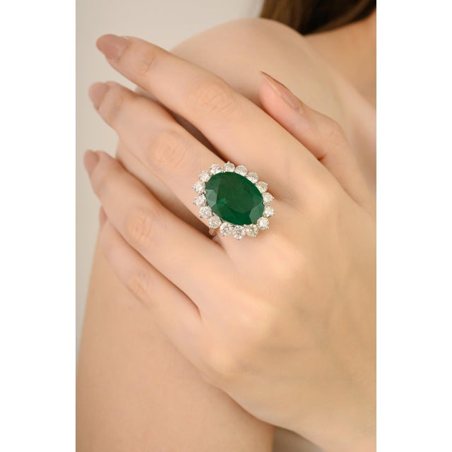 This luxurious cocktail ring showcases a certified 13.17 ct oval-cut emerald, surrounded by a 3.39 ct sparkling halo of...