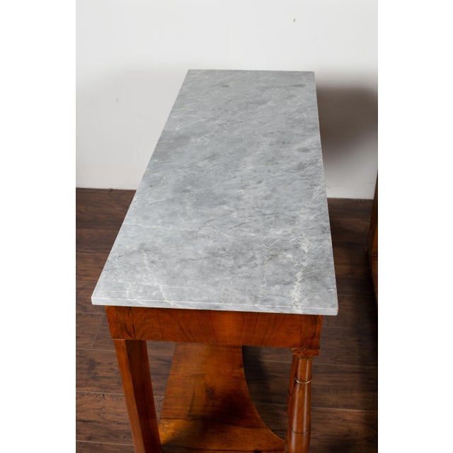 A pair of French Napoleon III period walnut console tables from the mid-19th century, with grey marble tops and bronze...