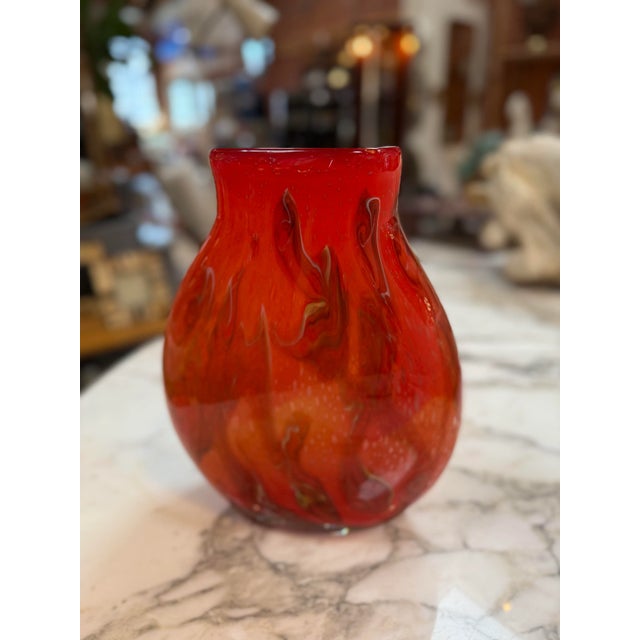 Handblown art glass murano vase featuring a vibrant fiery red and orange swirl pattern. The piece has a rounded, bulbous...