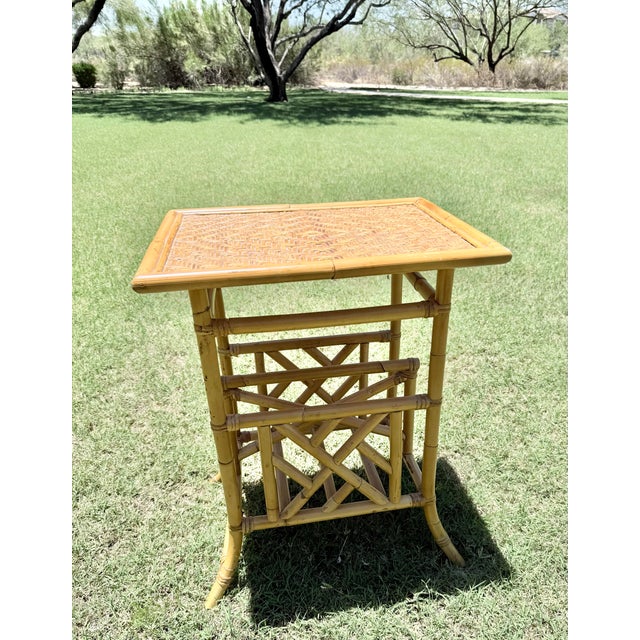 A charming vintage faux bamboo side table featuring a woven rattan top and an integrated magazine rack with decorative...