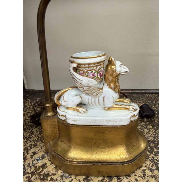 This is a unique porcelain lamp featuring a griffin with a floral painted urn between its wings. The linen shade looks...
