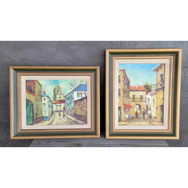 Two accompanying street scene oil paintings of a European town. Appears to be France. Painted on canvas with original...