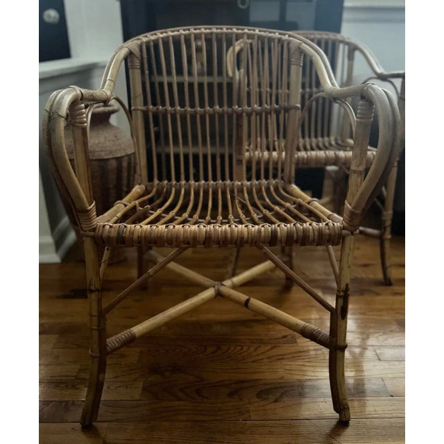 Pair of vintage 1970s rattan armchairs with arched backs and looped arms. Hand-wrapped cane details and warm patina add...