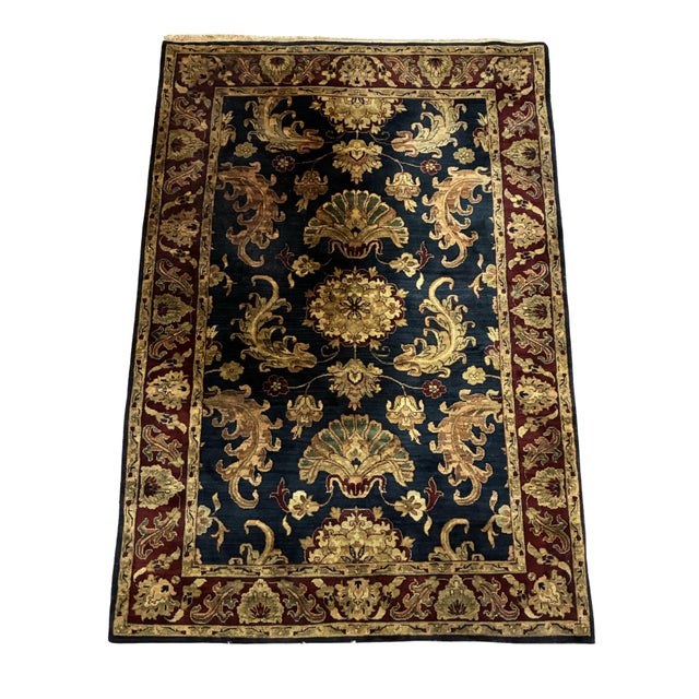 Hand-knotted area rug featuring a deep navy-blue field surrounded by a rich burgundy border. The design incorporates...
