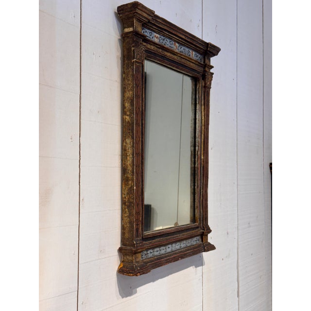 A rectangular Italian mirror with a stepped cornice, pilaster sides, and painted plaster panels featuring scrolling...