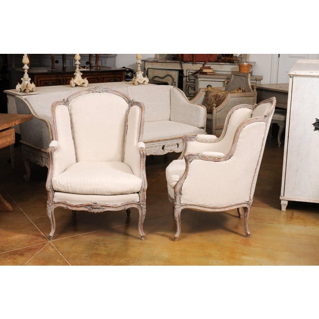 A pair of French Louis XV style painted wood bergères à oreilles chairs from circa 1880 with carved floral motifs,...