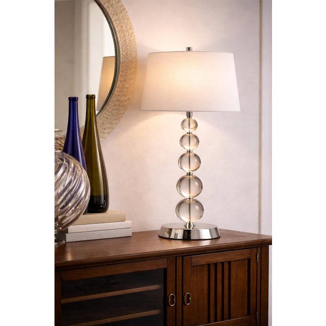 A striking modern glam table lamp featuring five stacked crystal or glass orbs on a polished chrome base, blending...