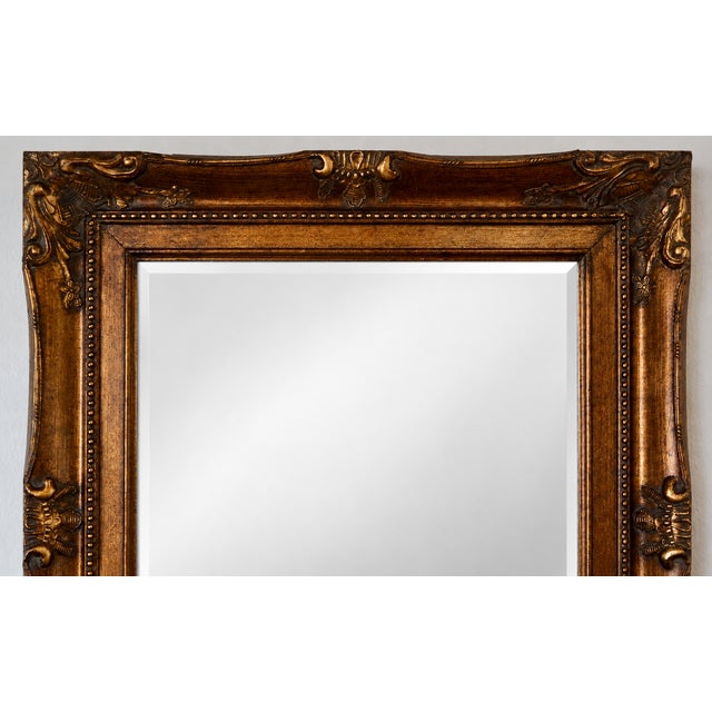 A large, substantial gilt mirror with a solid wood frame base and ornately detailed composition ornament — raised...