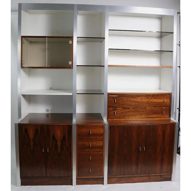 Stunning wall unit having rosewood cabinets with white Formica surfaces, brushed metal trim, and tinted glass shelves....