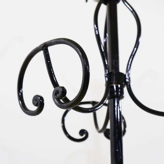Black wrought iron floor coat rack featuring elegant scrolls.