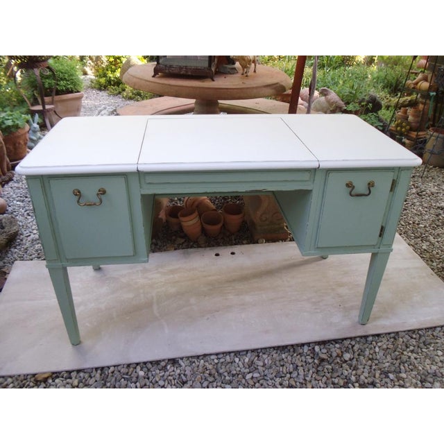 A vanity table from the 1960s, with a hinged center panel to which a mirror was probably once attached. The compartments...