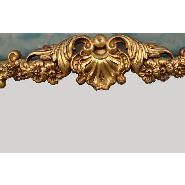 A dramatic vintage wall mirror featuring an elegant frameless silhouette accented with elaborate gilt Rococo-style floral...