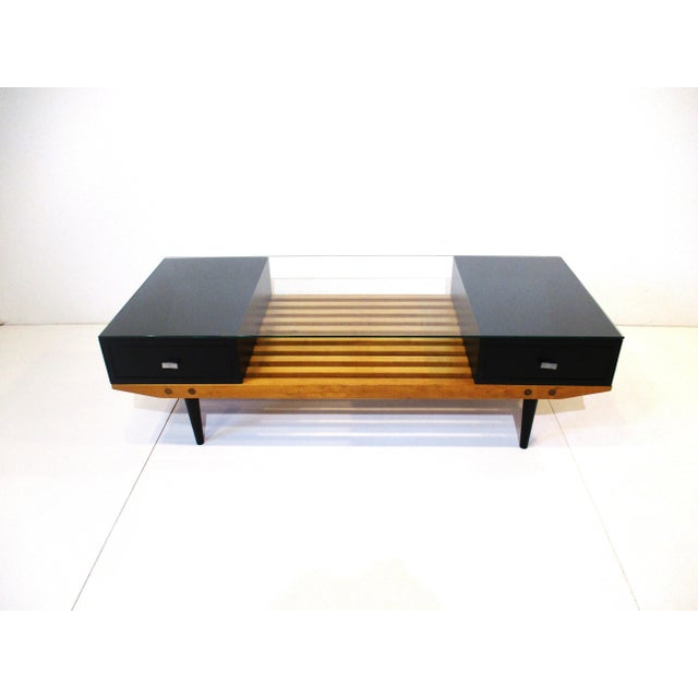A very well crafted solid maple slat wood coffee table with a satin black drawer to each end and a glass top spaning the...