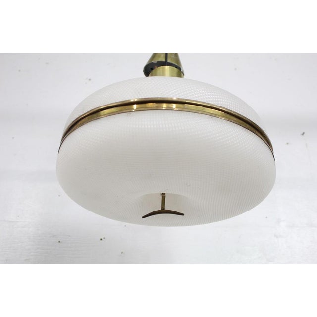 A Mid-Century Modern brass and plastic pendant light. The light has a rounded and patterned plastic shade in a waffle...