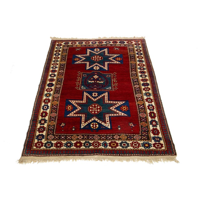 This Kazak wool rug is meticulously handcrafted and features a rich red palette adorned with delicate embellishments in...