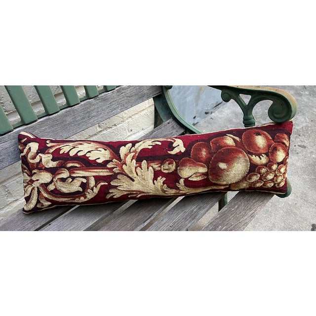 A beautiful pillow upholstered in 18th-century tapestry, featuring an elegant deep red ground adorned with richly detailed...