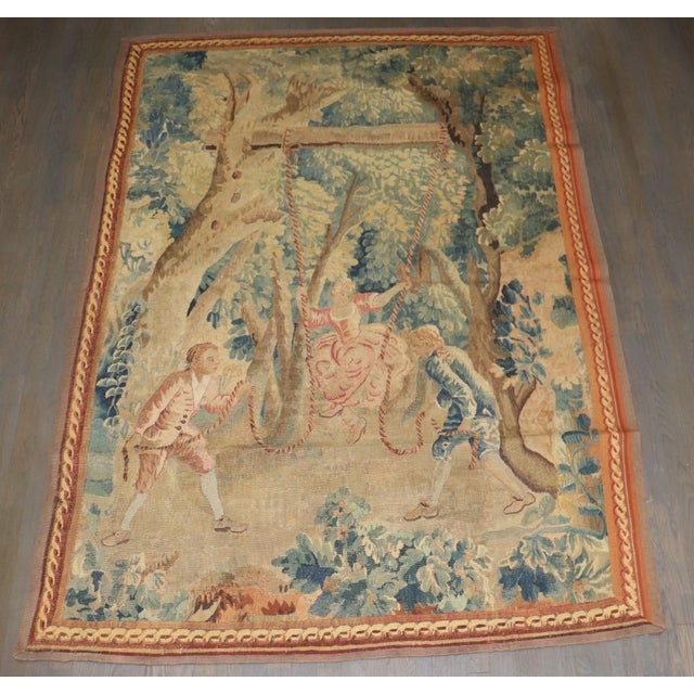 A Flemish rustic tapestry from the 18th century, depicting a charming scene with two young noblemen pulling a young damsel...