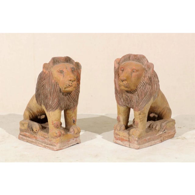 A pair of British colonial terracotta lions. This majestic pair of painted terracotta lions from the early 20th century...