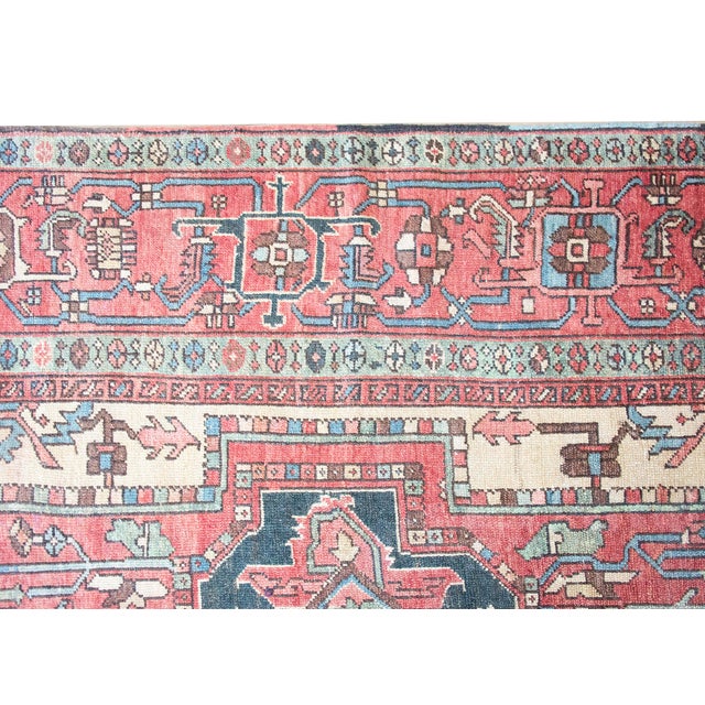 This early 20th-century Persian Heriz rug features a striking geometric medallion anchored on a rich terracotta field. The...